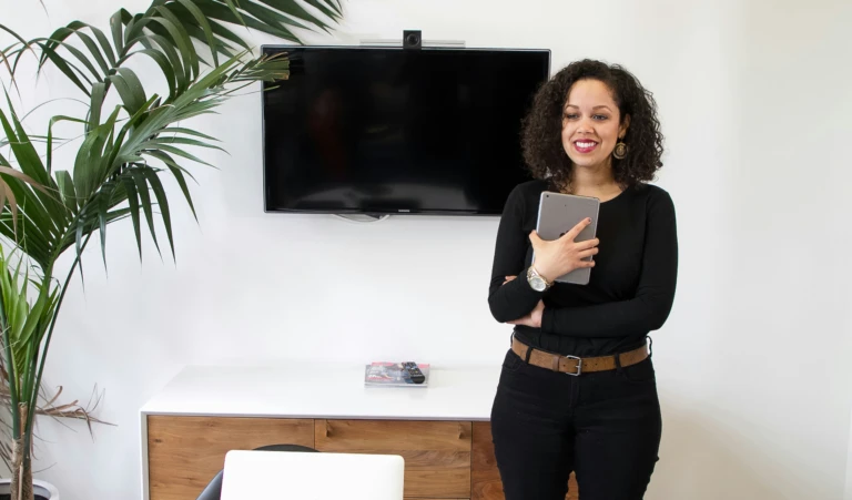 Woman standing at office desk, tablet in hand, focused on the screen.