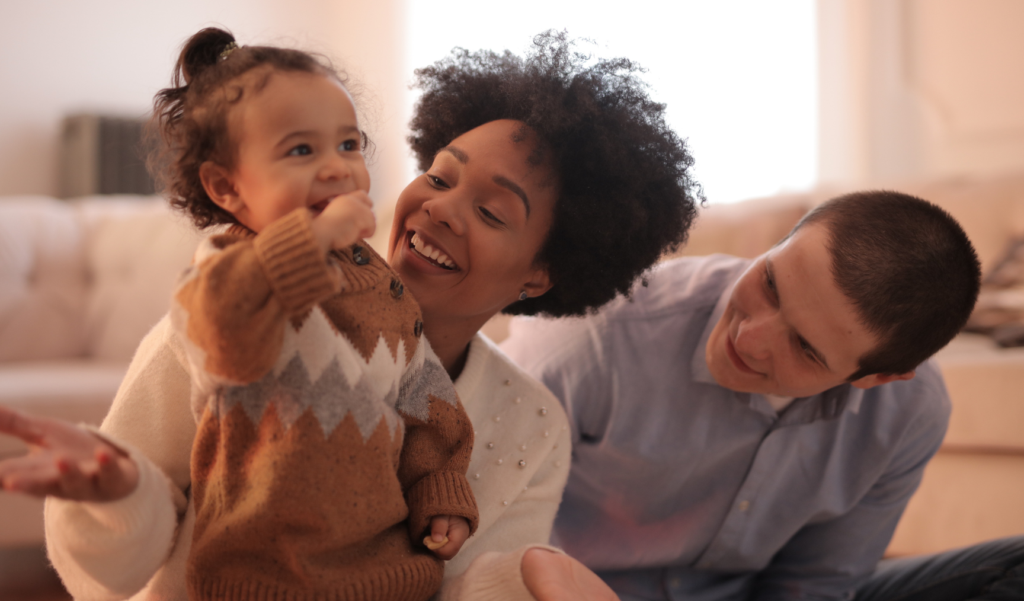 A man and a woman sit next to a toddler as she smiles