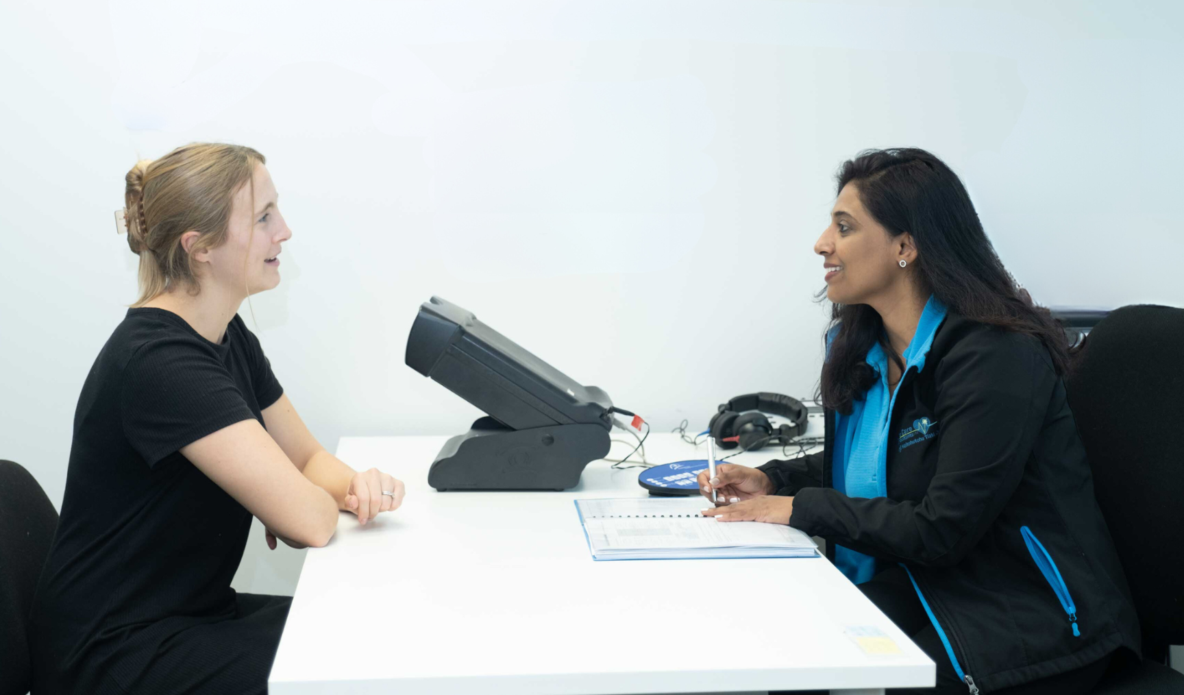Two women are sitting across from each other at a desk, engaged in conversation