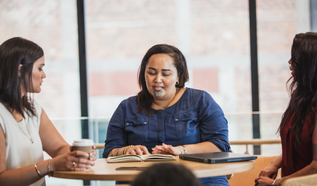 A Maori woman sits at a table in an office, discussing with two colleagues