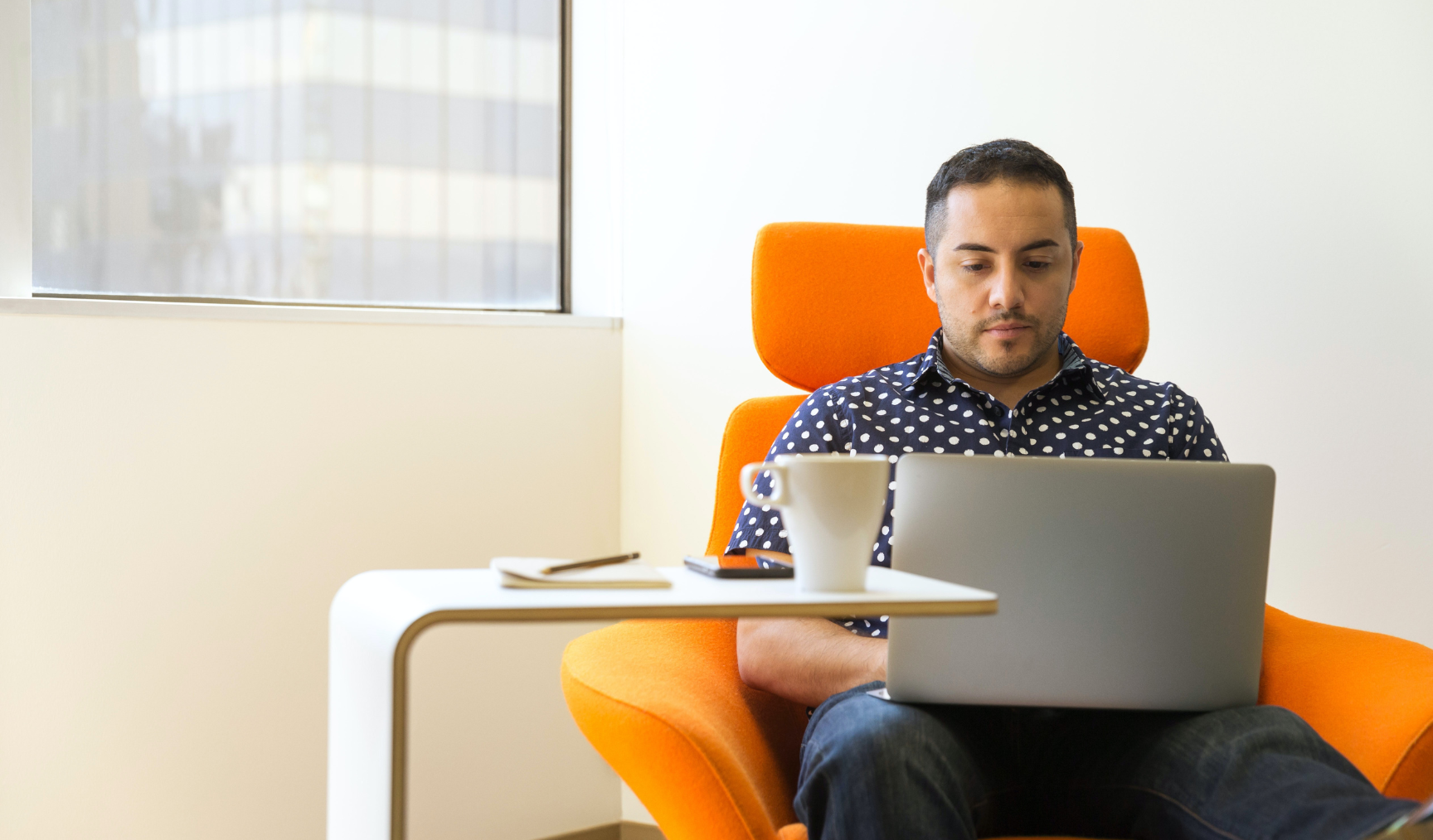 Man sits in comfortable armchair, typing on laptop