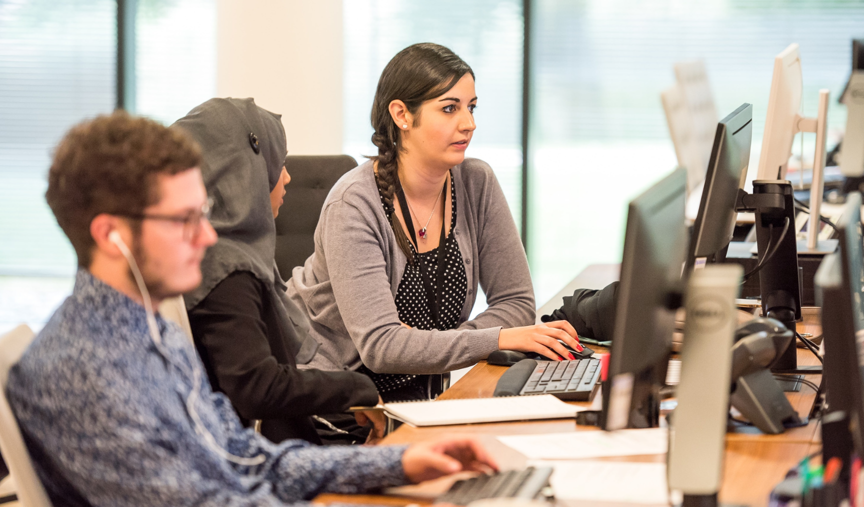 A couple of women look at a computer screen next to a man working on his own computer