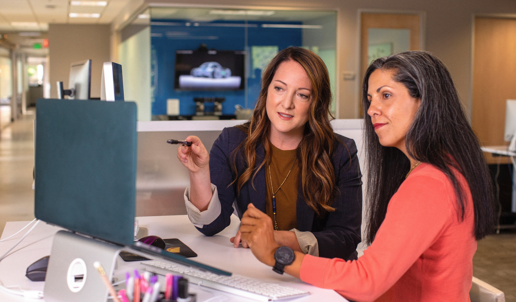 Two woman look at a computer screen, discussing between each other
