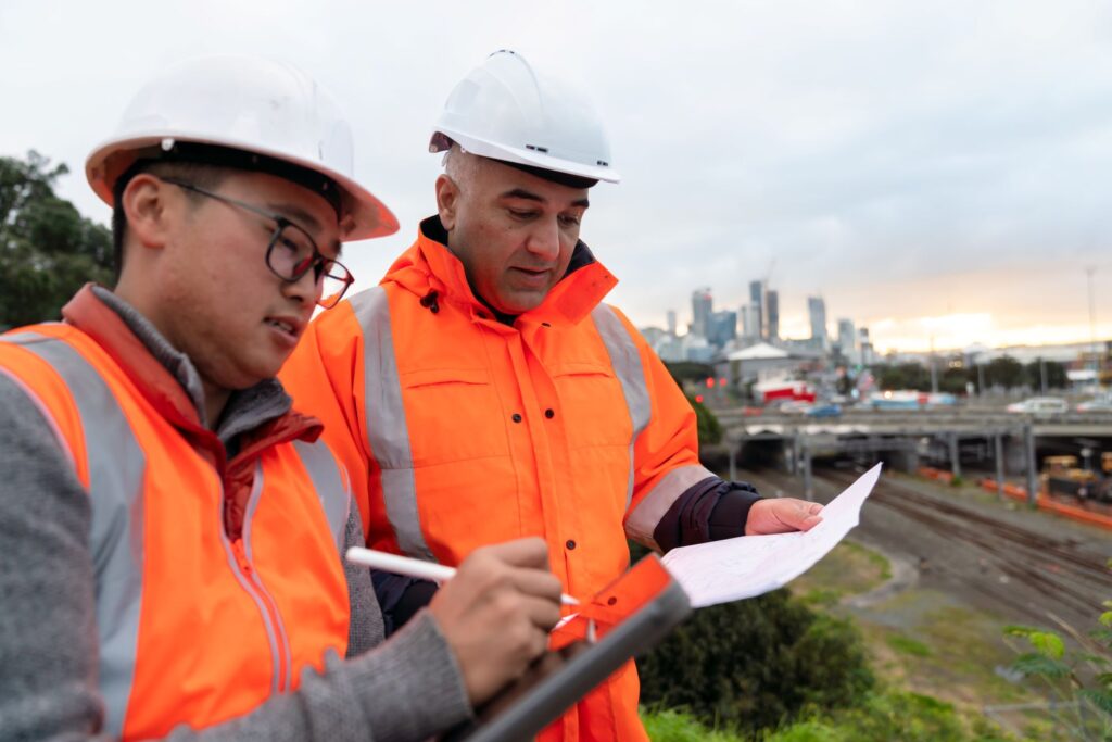 two male NZ construction employers standing side-to-side looking at paperwork