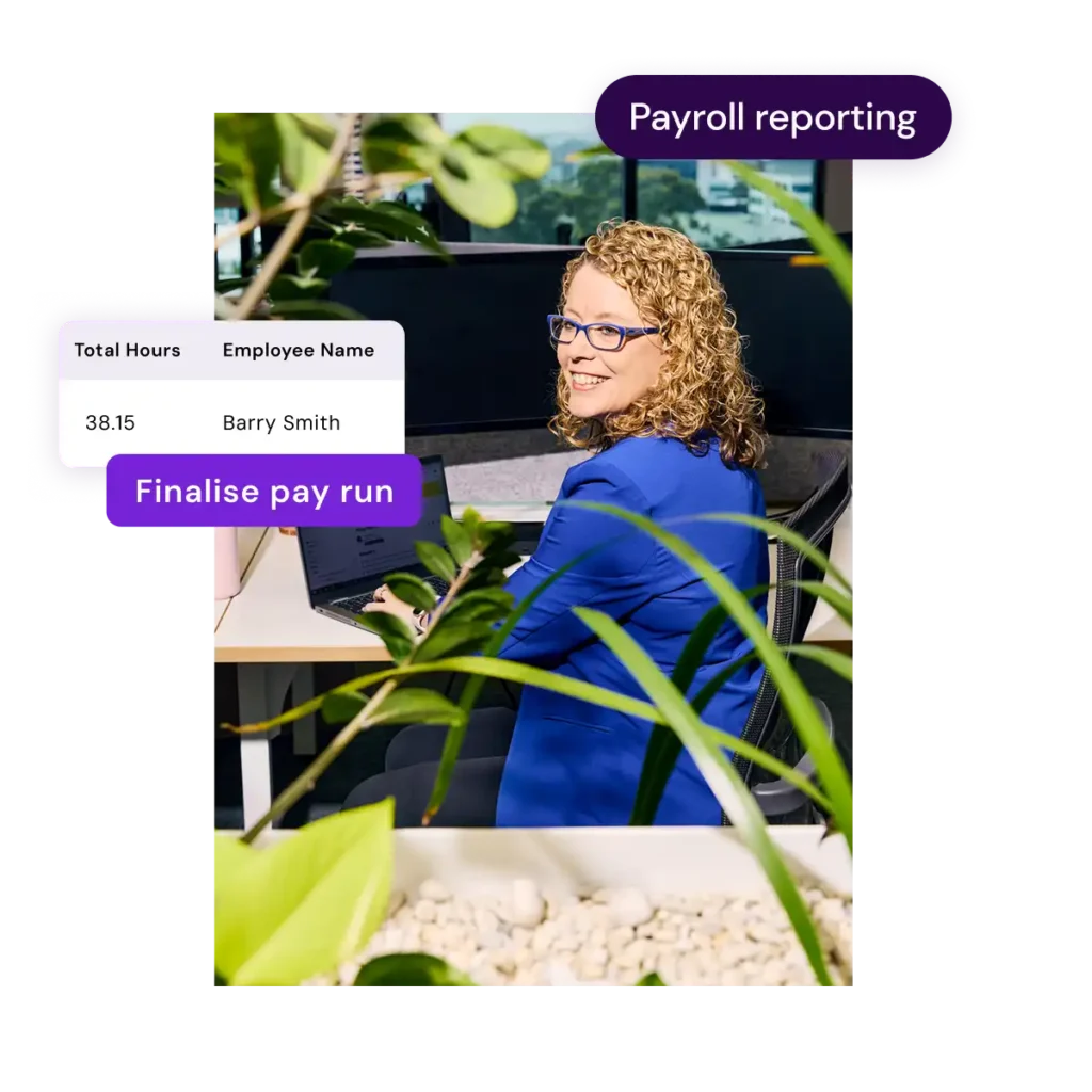 A professional woman with curly hair, wearing glasses and a blue blazer, smiles while working on a laptop in an office. Text overlays read "Payroll reporting" and "Finalize pay run." Plants on a desk and a window view create a lively atmosphere.