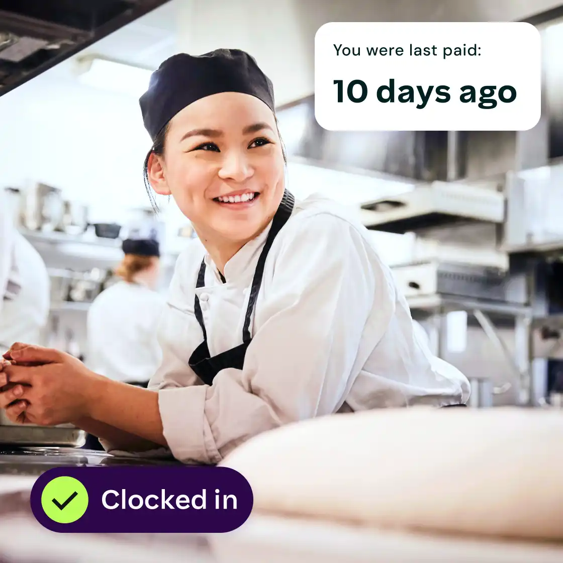 Smiling chef in a bustling kitchen, wearing a black cap and white uniform. Text overlay reads, "You were last paid: 10 days ago. Clocked in."
