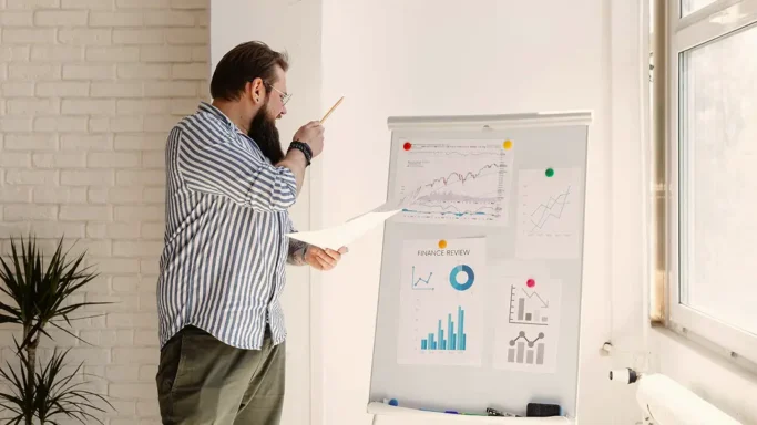 A man is presenting data on a flip chart with various graphs and charts displayed.