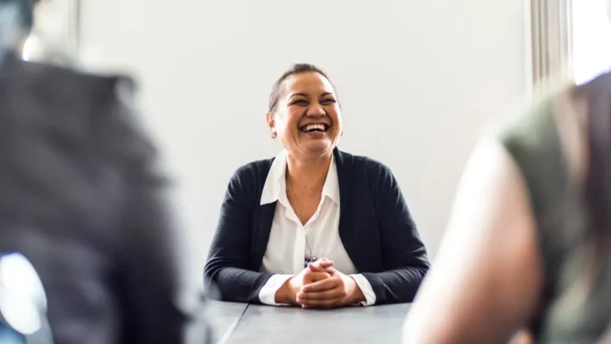 Smiling woman in business attire sitting at a table during a meeting.