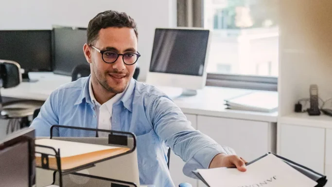 Smiling man in an office handing over a document.