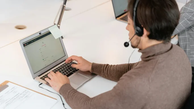 A person wearing a headset is working on a laptop at a desk.