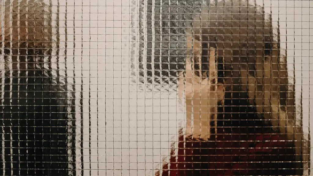 Two blurry figures seen through textured glass squares, one in black facing left and one in red facing right, creating a mysterious, abstract feeling.