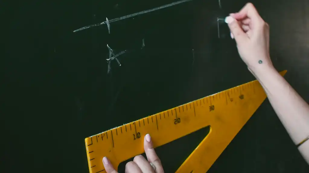 A hand drawing lines with chalk on a blackboard using a large yellow triangular ruler. The scene conveys focus and precision in a classroom setting.