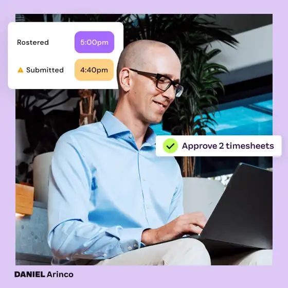 Bald man in glasses smiling while using a laptop. Notifications show timesheet approvals at 5:00 pm and 4:40 pm. Calm and focused atmosphere.