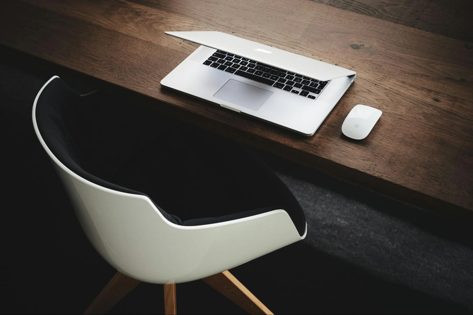 A wooden desk holds a laptop next to an empty chair, suggesting a work or study area.
