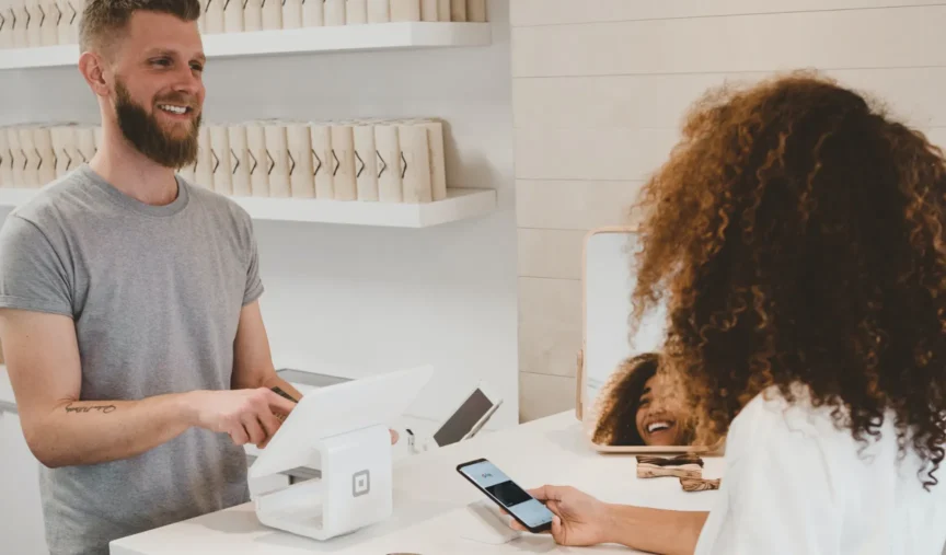 Barista smiling and assisting a customer with a payment at a café counter.