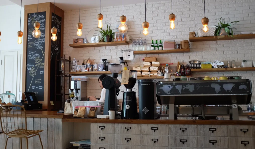 Cozy café interior with people working behind the counter and warm hanging lights.