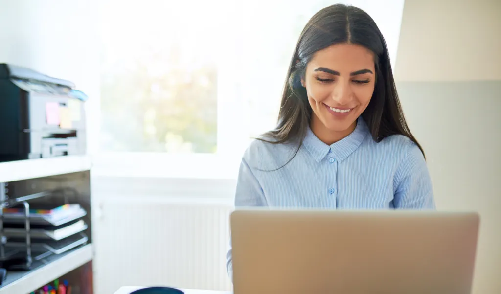 An image of a woman working on her laptop in a sunlit room
