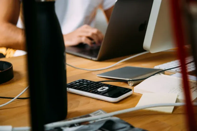 A calculator and laptop on a desk while a person types, illustrating the traditional financial tasks that AI in accounting can help employers automate.