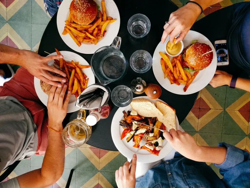 A top-down view of friends sharing burgers and meals at a table, representing the customer dining experience that AI in hospitality can help employers enhance.