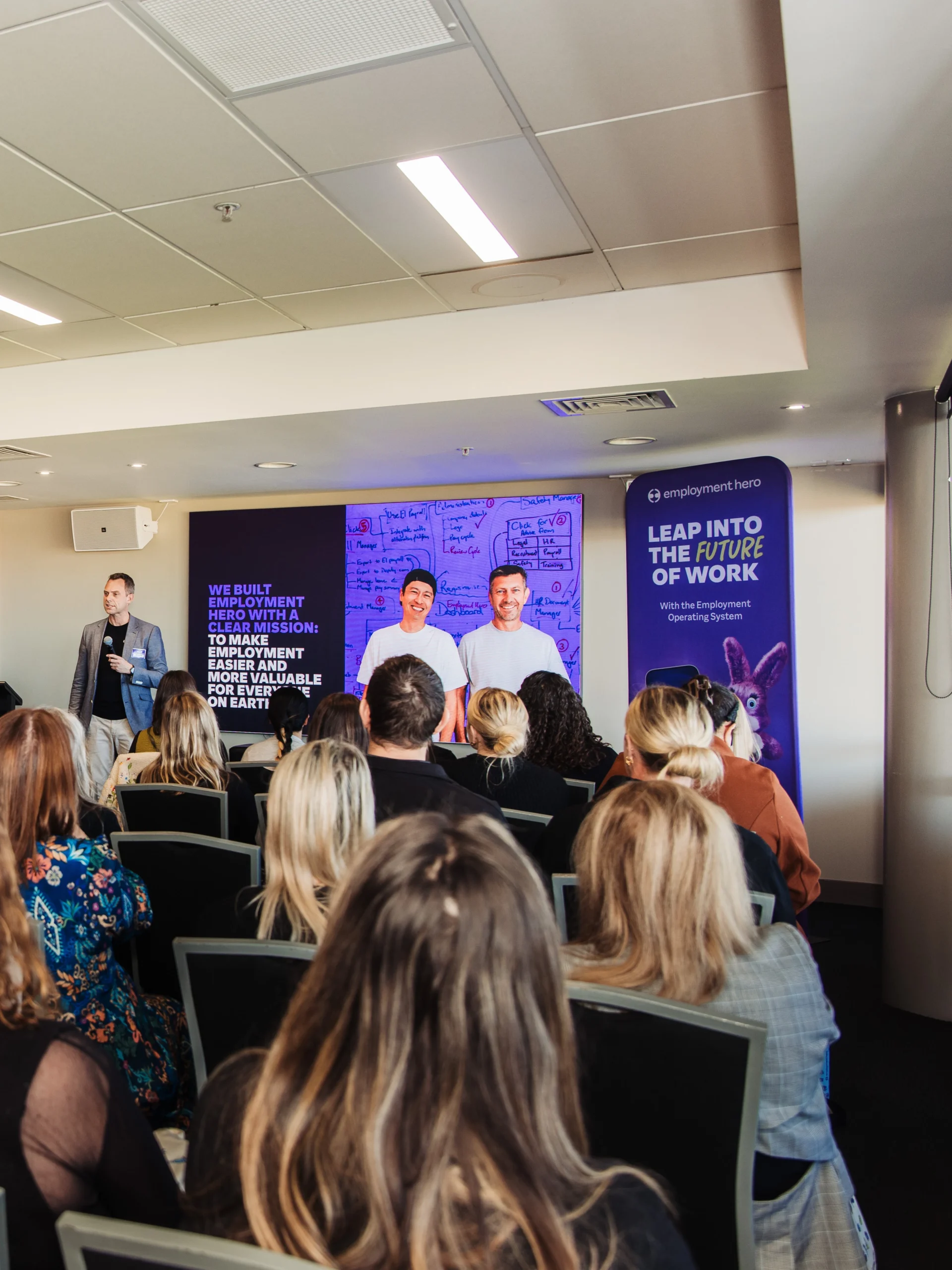 Employment Hero corporate presentation with speakers on stage addressing a seated audience at a future of work seminar.