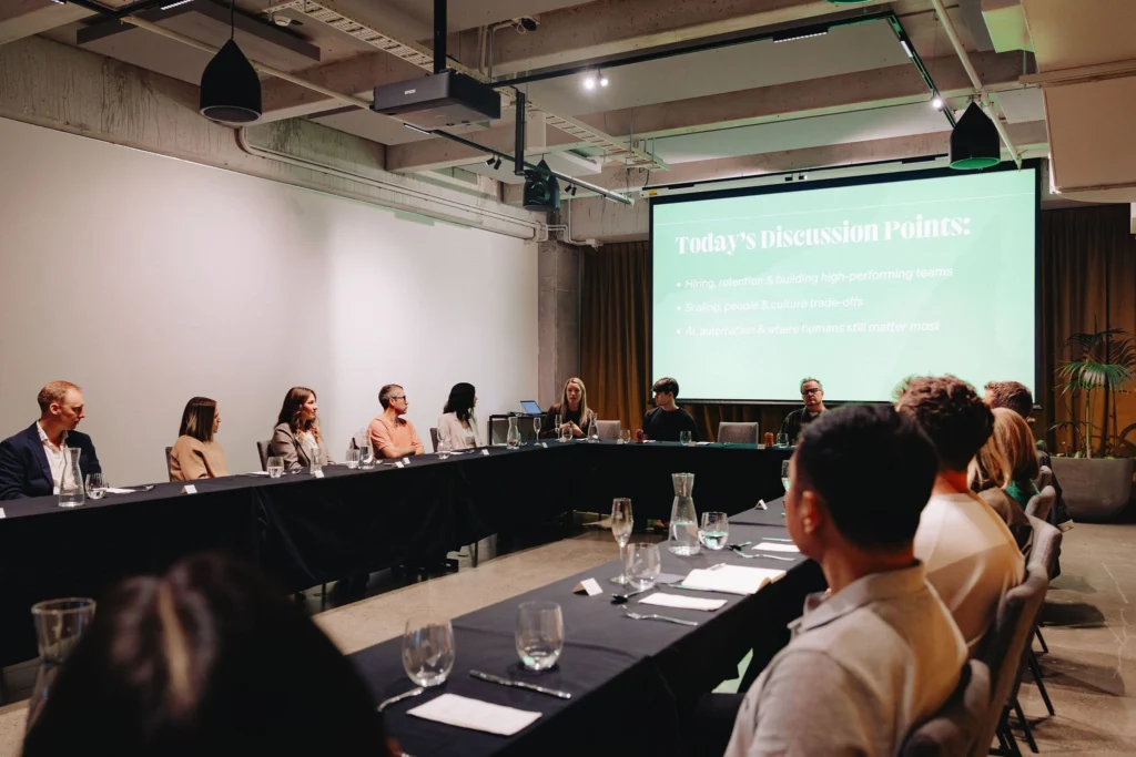 A group of people seated around a U-shaped table in a conference room, engaging in discussion. A projector displays "Today's Discussion Points."