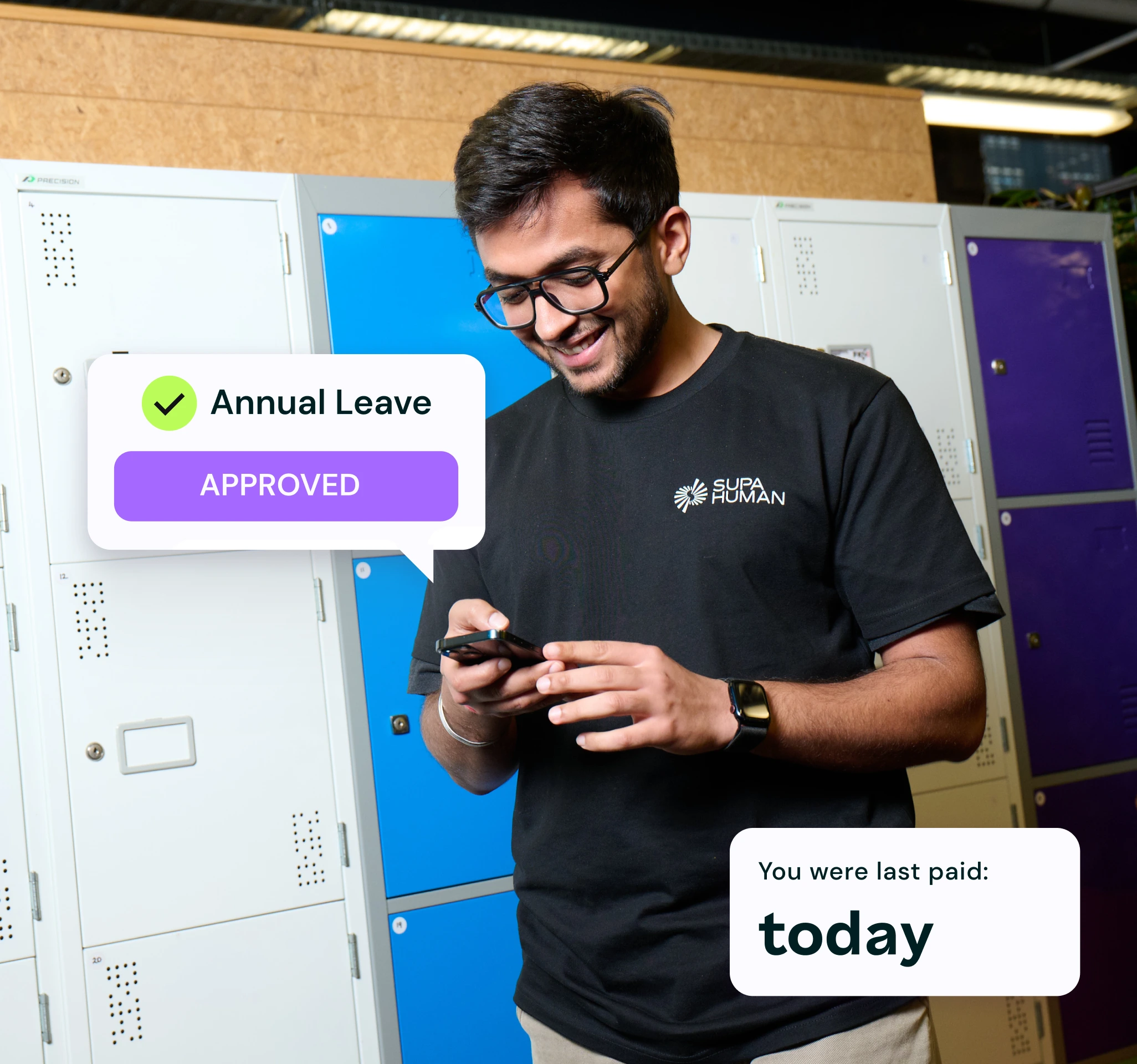 Man in casual attire smiles while checking his phone in front of blue and white lockers. Notifications show "Annual Leave Approved" and "You were last paid: today."