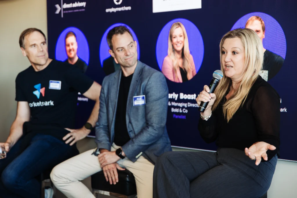 Panelists sit on stage as a blonde woman speaks into a microphone during a professional Employment Hero presentation event.