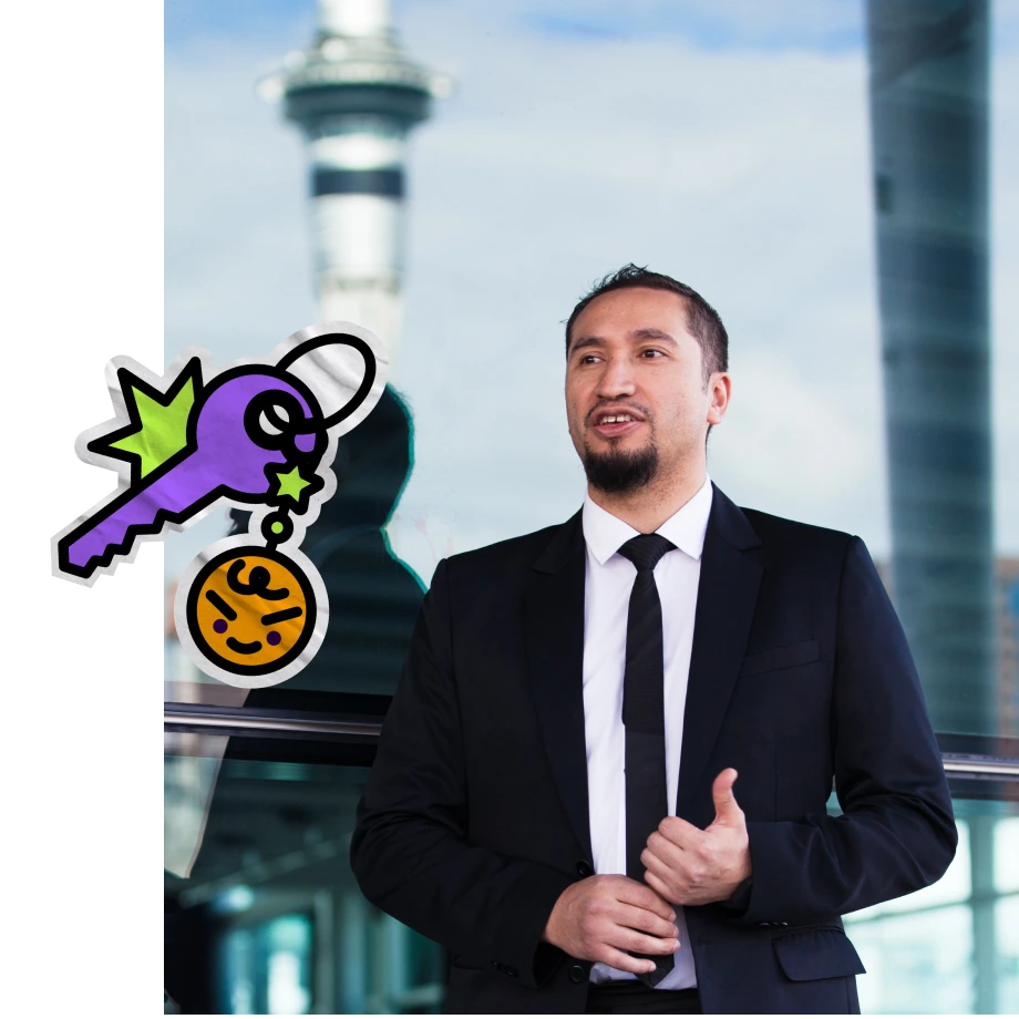 A professional man with a goatee wearing a black suit and tie stands in front of a glass window, with the Auckland Sky Tower clearly visible in the background. A cartoonish graphic of a purple key with an orange face keychain is overlaid on the left side of the image.