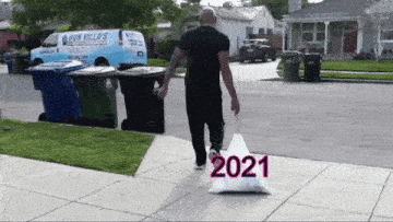Man dragging garbage bag labelled '2021' to the dumpster