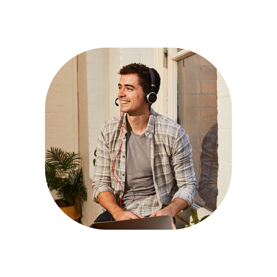 An image of a man casually sitting down, smiling with headphones on