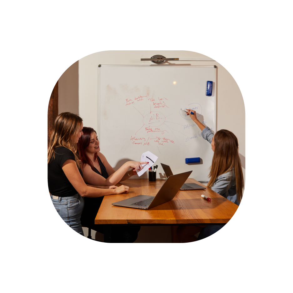 An image of a woman writing on the whiteboard, discussing to two more women