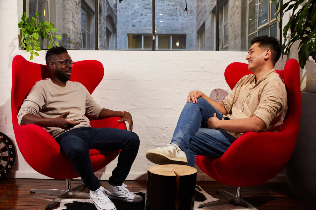 Two men sitting on red chairs having a friendly discussion