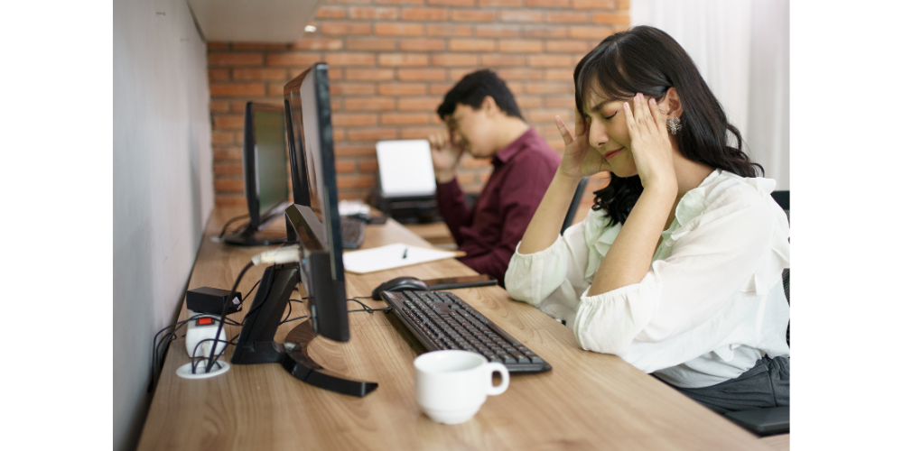A lady sat with her head in her hands at a desk next to a colleague
