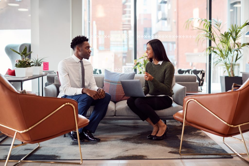 Two people sat on sofa in office talking.