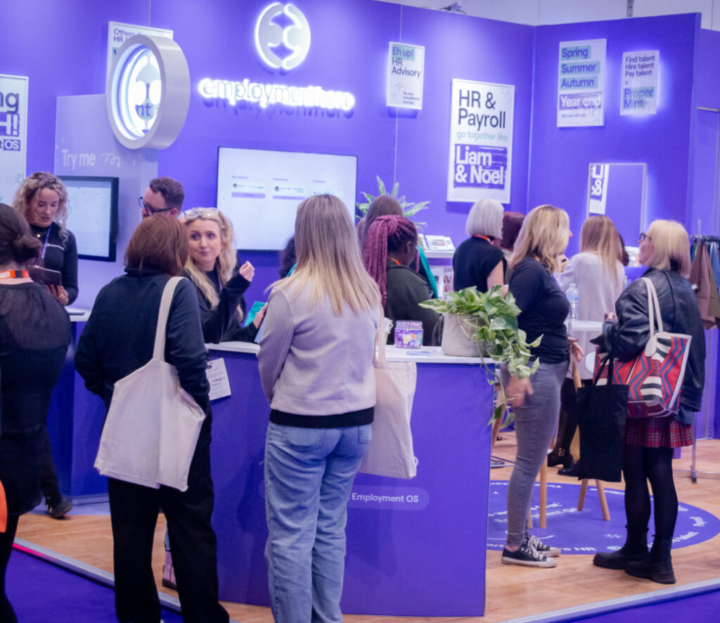 People gather and converse at a vibrant exhibition booth with purple decor and digital displays during a tech or business event