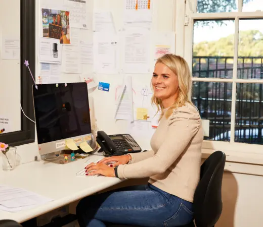 Woman at desk smiling while typing on a computer.