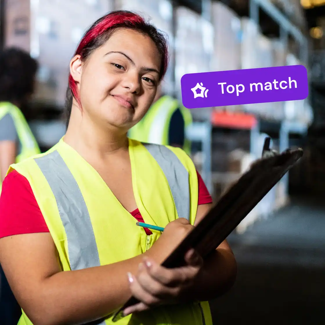 A woman with red hair smiles, wearing a yellow safety vest, holding a clipboard in a warehouse. A "Top match" badge appears nearby, conveying confidence.