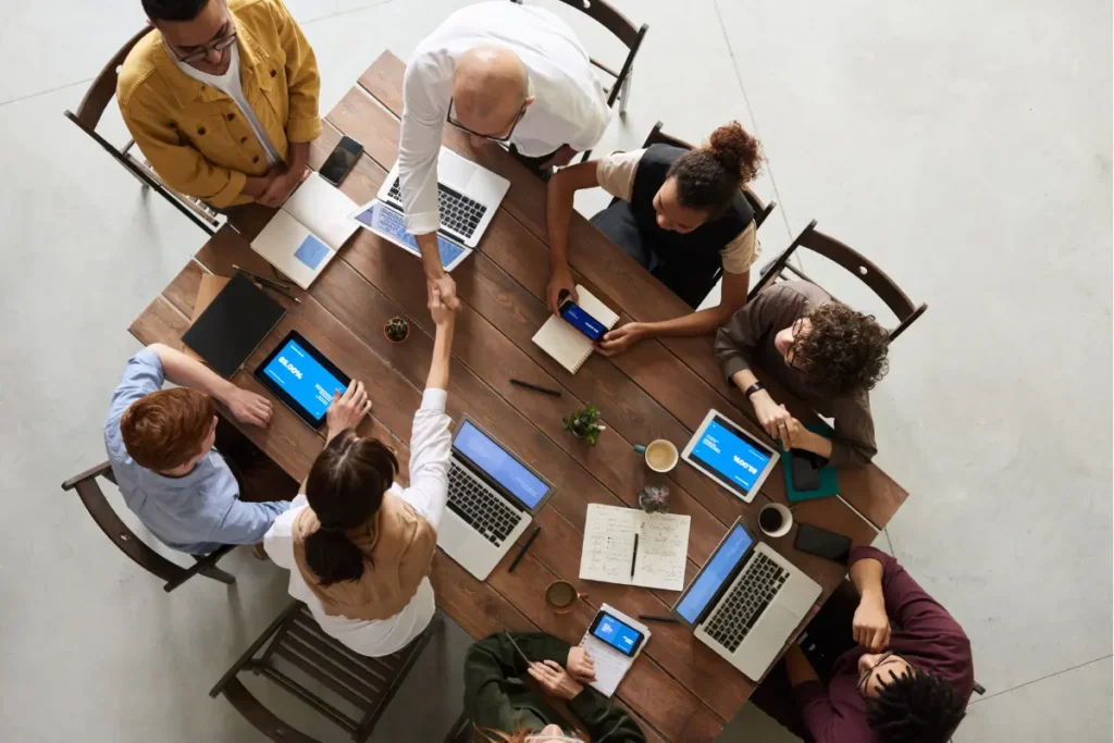 Team of diverse professionals collaborating in a business meeting around a table with laptops, tablets, and notebooks