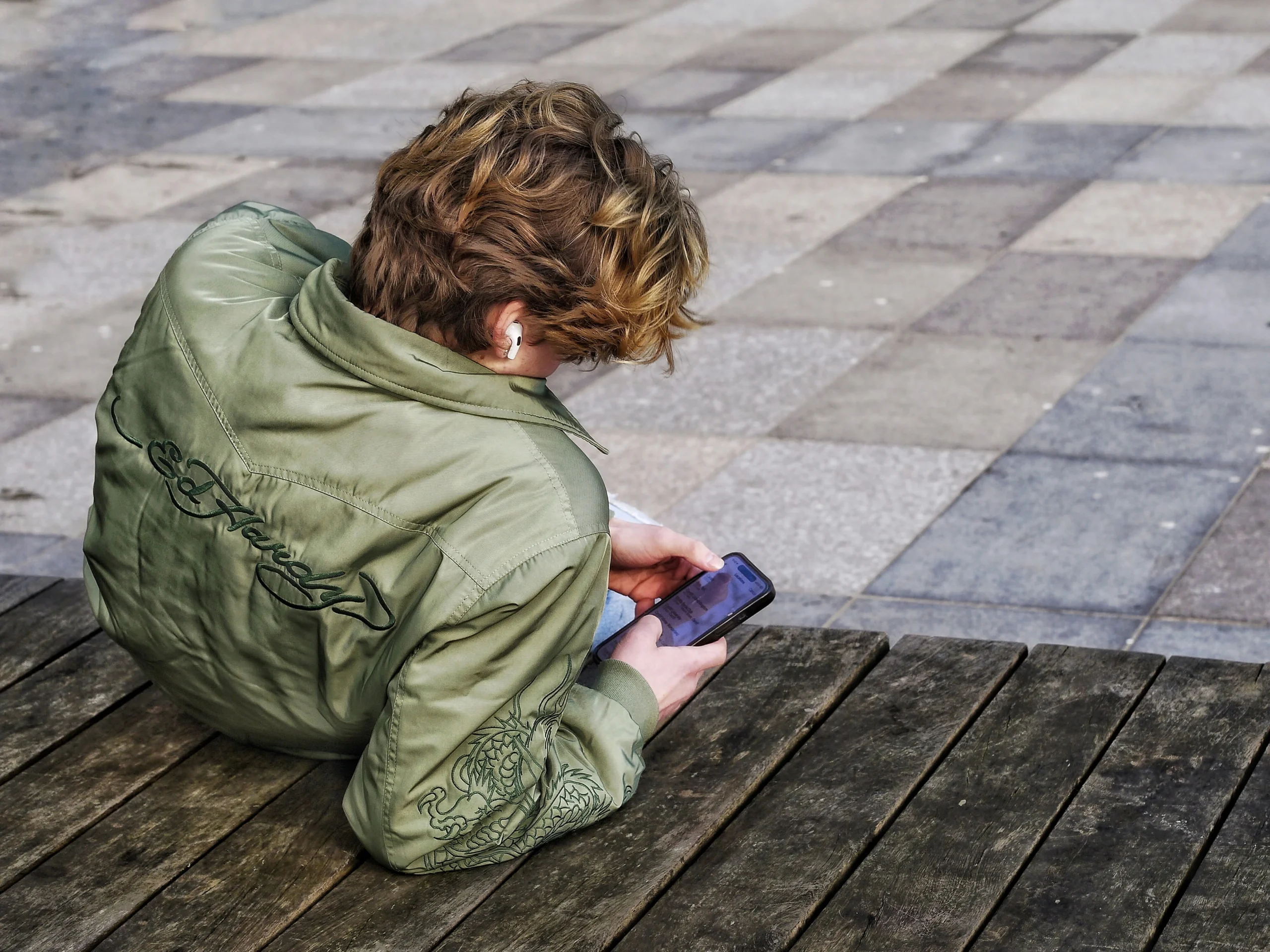 A man sitting on a wooden bench in a park, focused on his phone.