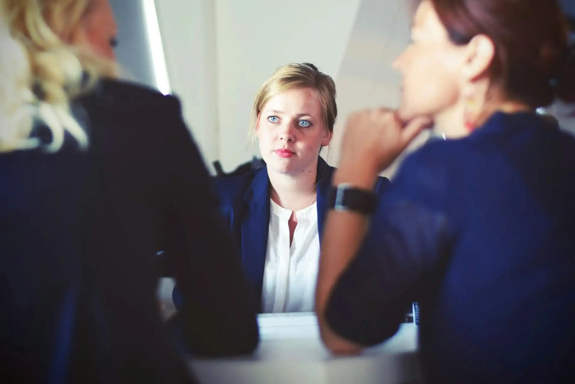 Three professionals in suits engage in a serious discussion. The woman in the middle listens intently, creating a focused and contemplative atmosphere.