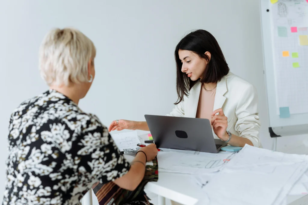 Two professional women reviewing business plans and documents during a collaborative meeting in a modern office.