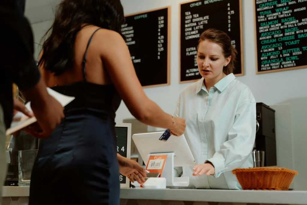 Customer handing credit card to cashier at café counter with visible food and drink menu