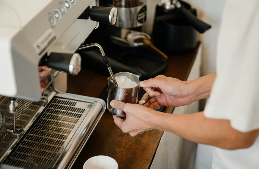 Person frothing milk with steam wand on espresso machine for coffee preparation