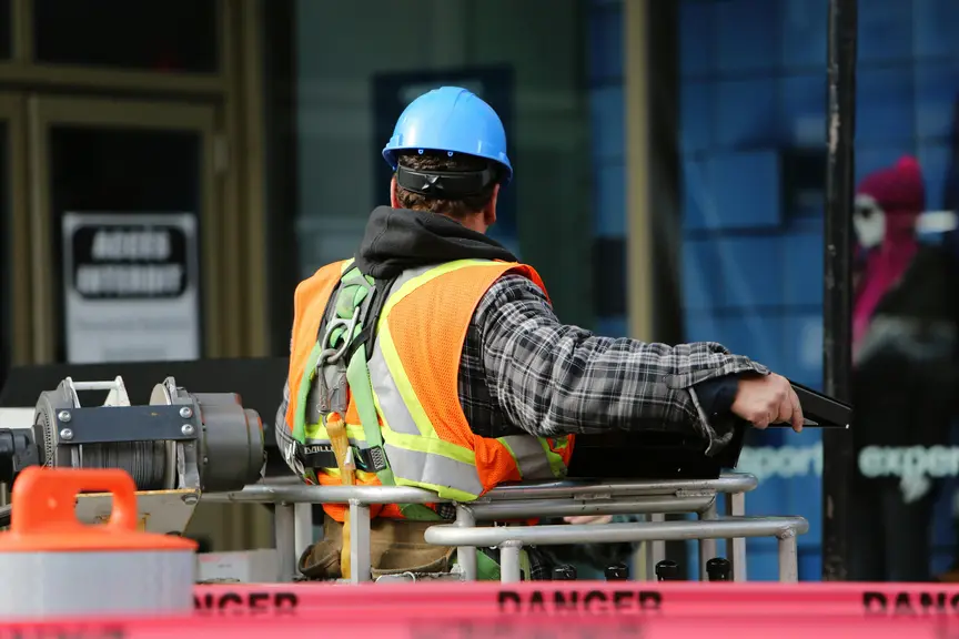 Construction worker wearing a hard hat and high-visibility vest operating equipment at a worksite.