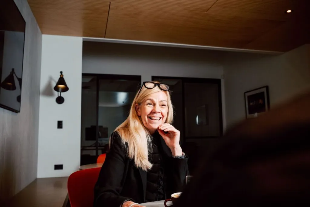 A blonde woman with glasses on her head smiling during a conversation in a modern office.