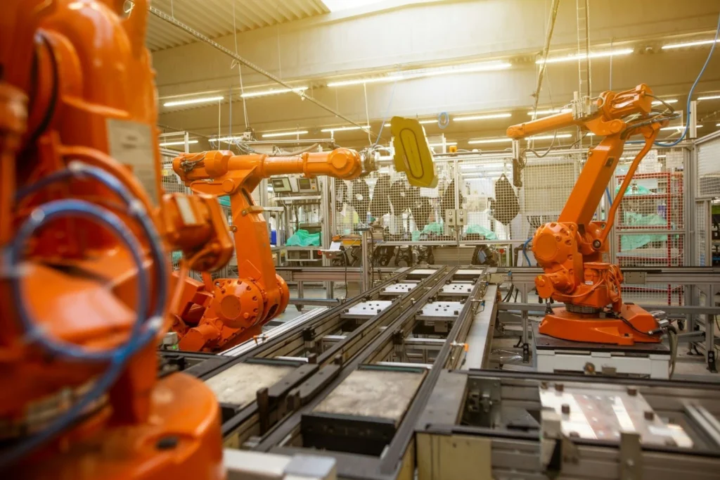 Robotic arms in a factory setting work on an assembly line. The orange machines are engaged in precise tasks, conveying a sense of efficiency.