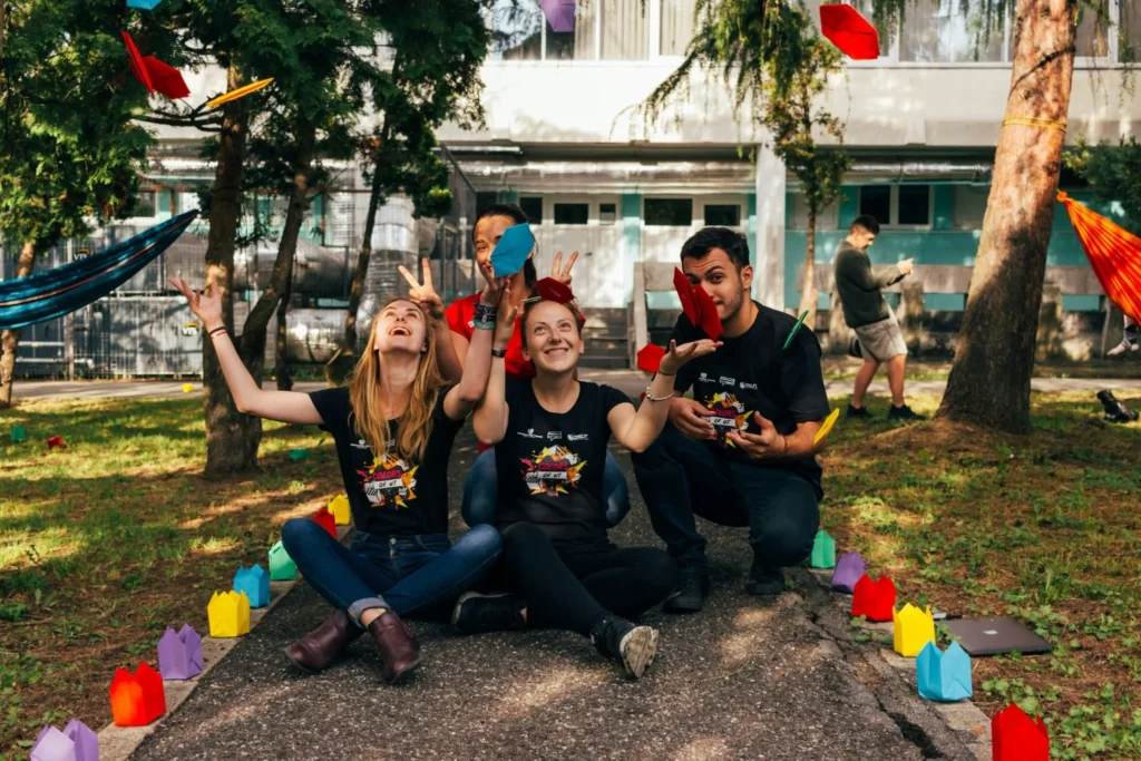 A joyful group of non-profit team members throwing colorful paper shapes into the air outdoors, highlighting the positive impact and time saved when leaders successfully implement AI for non-profit organisations.