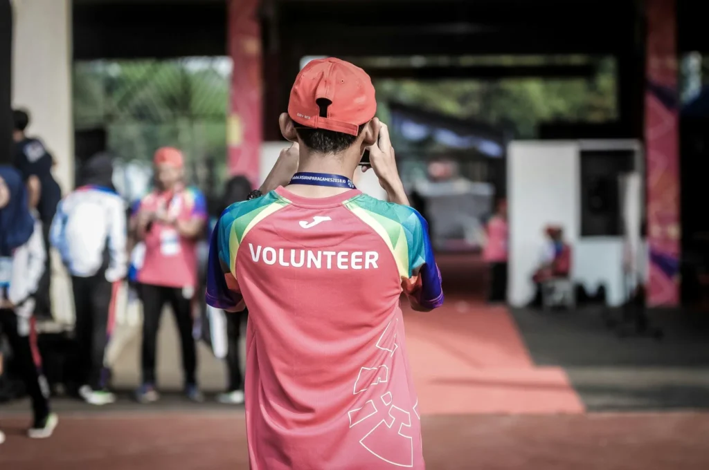 A volunteer wearing a bright red shirt taking a photo at a community event, illustrating how UK non-profit leaders can use AI tools to streamline volunteer management and community engagement.