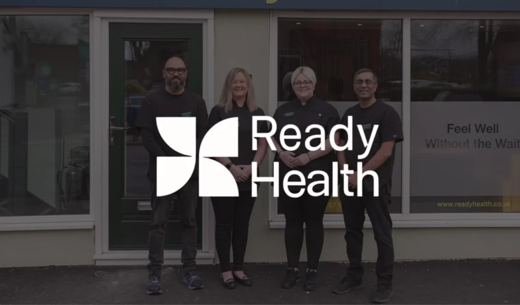 Four people stand smiling outside a building with a "Ready Health" sign, conveying a welcoming atmosphere. They are in front of large windows.