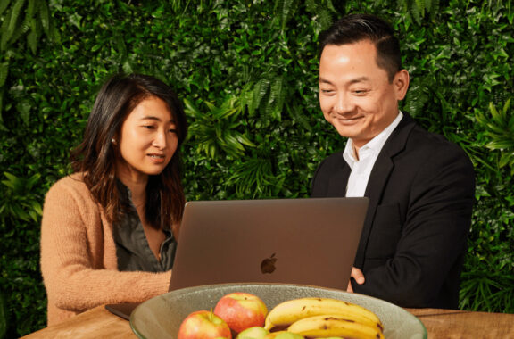 two colleagues sitting at a table looking at the same laptop against a vertical garden wall